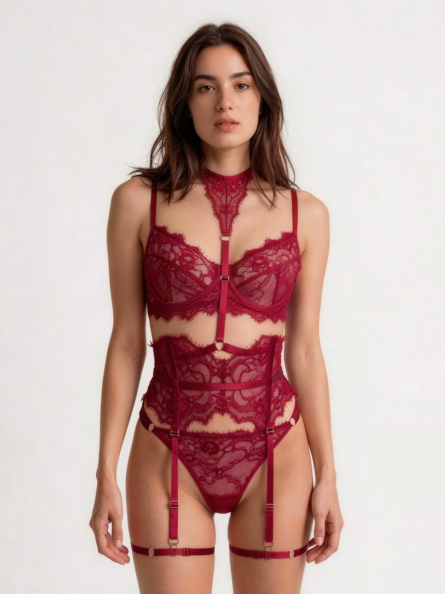 A woman modeling a deep burgundy lace lingerie set with a high-neck choker, underwire bra, bodysuit, matching panties, and garter straps against a plain white studio background.