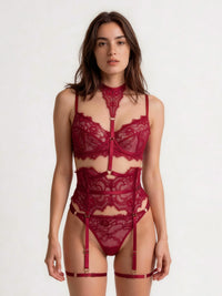 A woman modeling a deep burgundy lace lingerie set with a high-neck choker, underwire bra, bodysuit, matching panties, and garter straps against a plain white studio background.