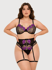 A plus-size model wearing a black lace lingerie set with purple floral embroidery, including a bra, high-waisted briefs, and garter straps, against a light gray background.