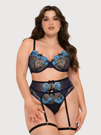 A woman modeling a three-piece lingerie set featuring a navy blue and black sheer mesh bra, matching high-waisted garter belt, and panty with light blue floral embroidery, set against a solid light gray background.
