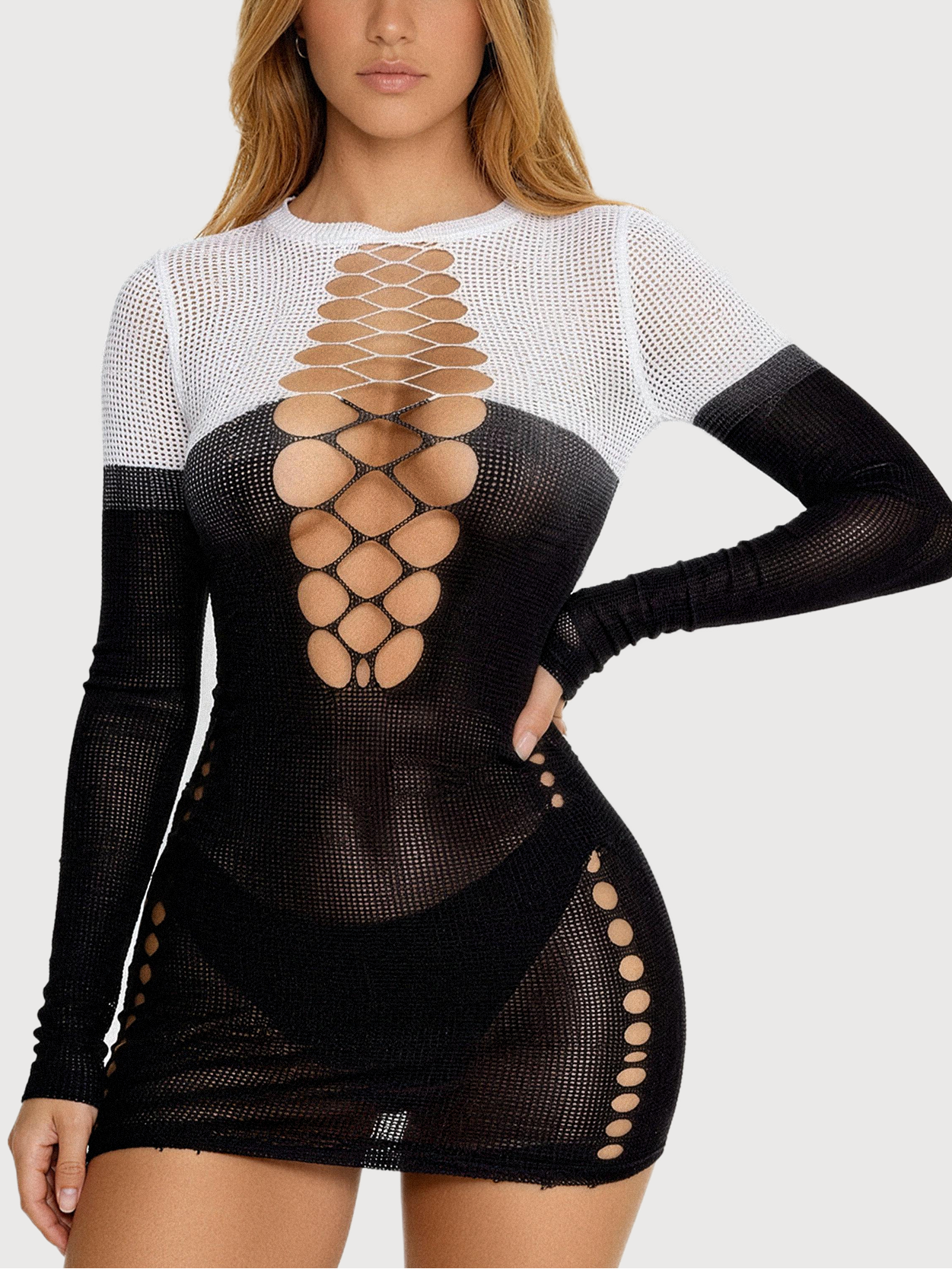 A woman modeling a long-sleeve black mesh mini dress with a white mesh yoke and a large central cutout pattern on the torso, against a light gray studio background.