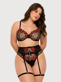 A woman modeling a black sheer lingerie set with red rose embroidery, including a bra, high-waisted briefs, and garter straps, against a light gray background.